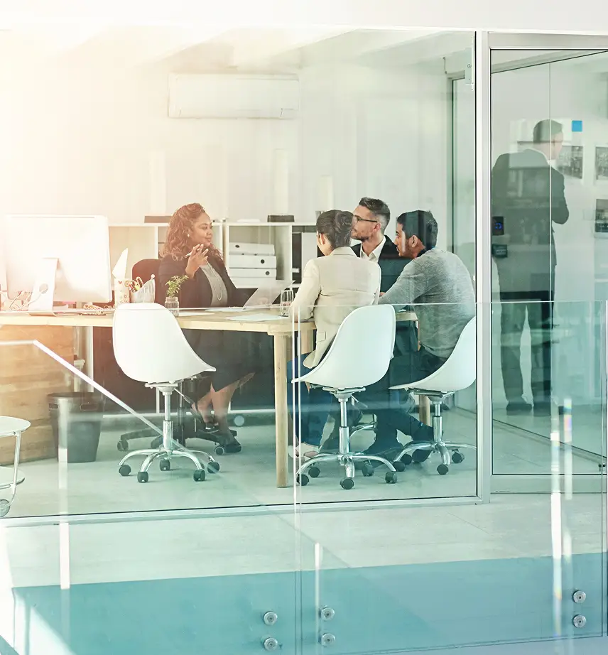 4 office workers inside glass walled board room